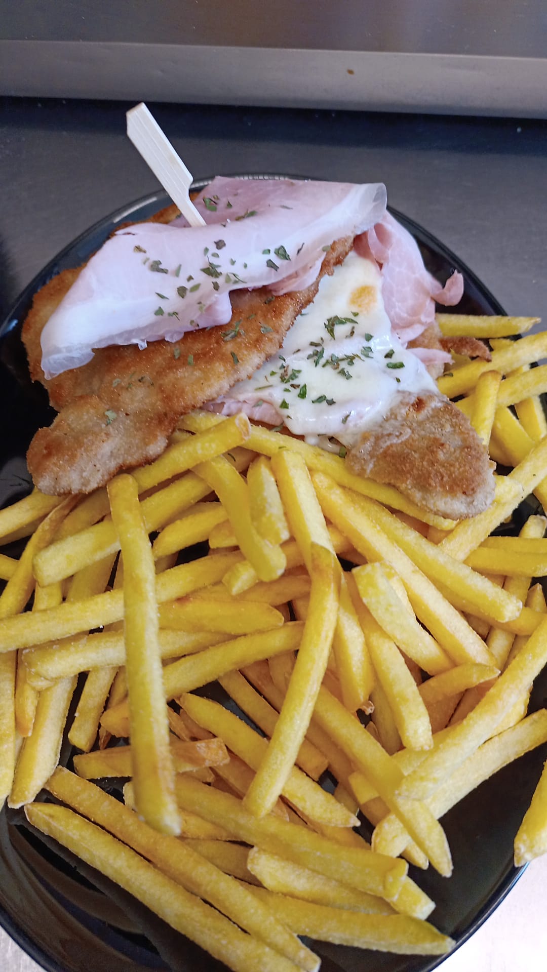Ein Teller mit Pommes frites, Schnitzel, Schinken und cremiger Sauce, garniert mit gehackter Petersilie.