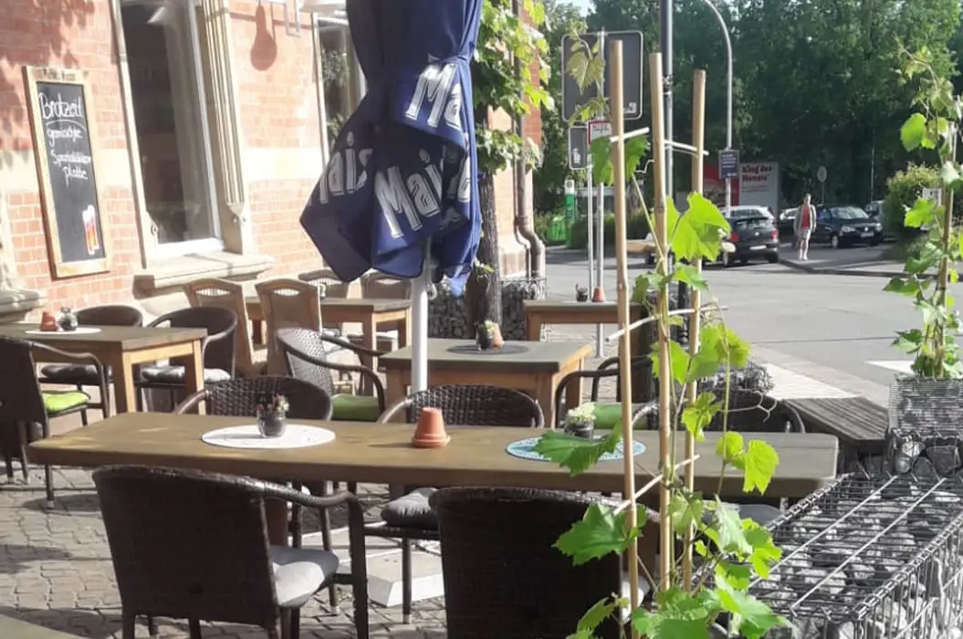 Sonnige Terrasse eines Cafes mit Holztischen Korbstuehlen und blauem Sonnenschirm